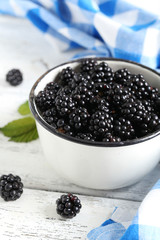 Fototapeta na wymiar Beautiful ripe blackberry in cup on white wooden background