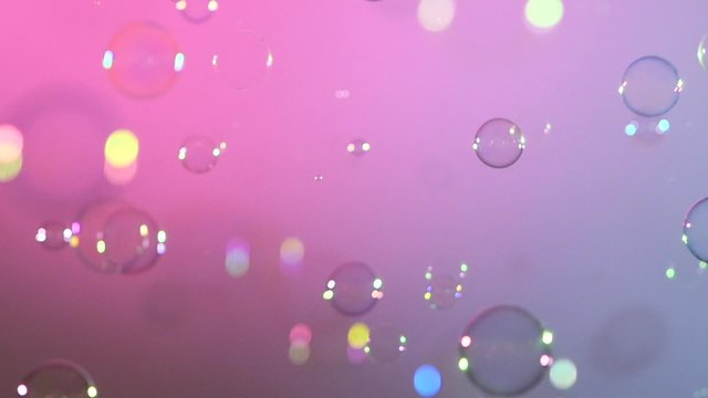Blue and clear soap bubbles on pink and violet, background, slow