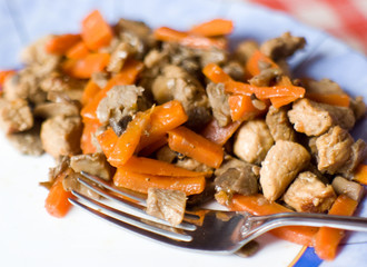 Metal fog on a plate with chineese ragout made of pork, carrot and mushrooms on a ceramic plate
