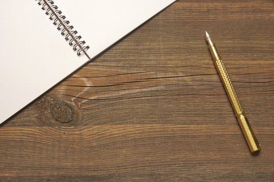 Open Spiral Bound Notebook With White Pages And Gold Pen.