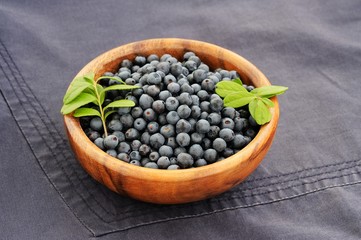 Fototapeta na wymiar Fresh wild blueberries with green leaves in handmade wooden bowl