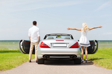 happy man and woman near cabriolet car at sea