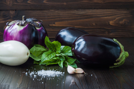 Purple and white eggplant (aubergine) with basil and garlic on dark wooden table. Fresh raw farm vegetables - harvest from the garden in rustic kitchen. Rural still life