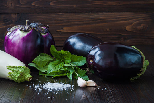 Purple and white eggplant (aubergine) with basil and garlic on dark wooden table. Fresh raw farm vegetables - harvest from the garden in rustic kitchen. Rural still life