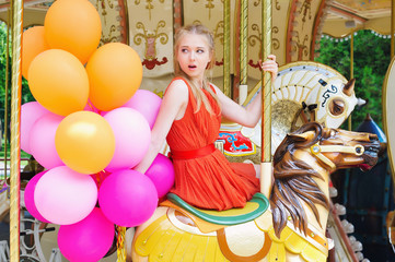 Fototapeta na wymiar Lifestyle concept, attractive teenager with colorful latex balloons in the amusement park riding a carousel