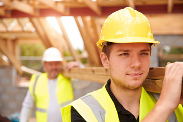 Builder And Apprentice Carrying Wood On Construction Site