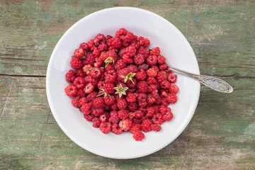 fresh red raspberry lies in a plate with a spoon on the old wooden table with peeled paint