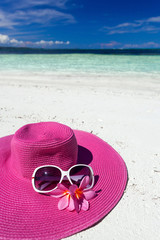 Pink summer hat on beach with sunglasses and plumeria