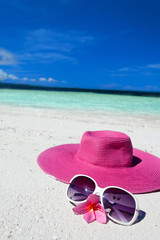Pink summer hat on beach with sunglasses and plumeria