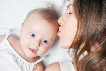 Happy mother with a baby lying on a white bed
