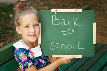 Little girl holding Chalkboard with words Back to School. Outdoor photo