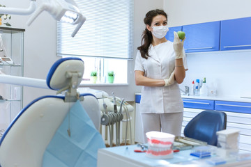 Dentist in mask holding green apple.