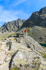 Fototapeta premium Young woman tourist standing on top of rock on hiking trail in summer landscape of High Tatra Mountains, Slovakia