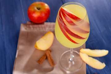 Glass of apple cider with fruits and cinnamon on table close up