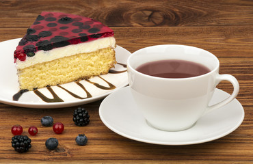 A piece of cheesecake with berries and a cup of tea on the wooden background.