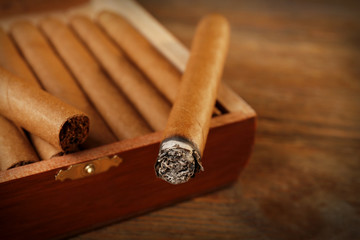Cigars and burning one on wooden table, closeup