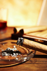 Cigars and burnt one with ash on wooden table, closeup