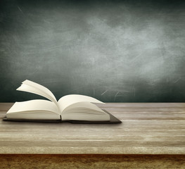 Open book on table in front of blank chalkboard. Copy space