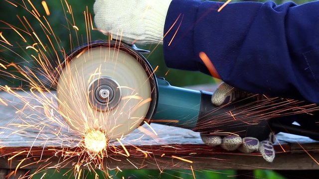 Worker in gloves cutting a metal pipe in two pieces with angle grinder

