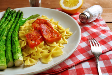 Roasted asparagus and tasty pasta with vegetables on plate on wooden table background