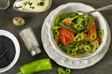 Roasted asparagus and tasty colorful pasta with vegetables, spices in bowl on colorful background