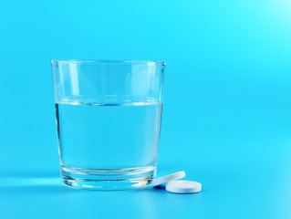 Glass of water and pills on blue background