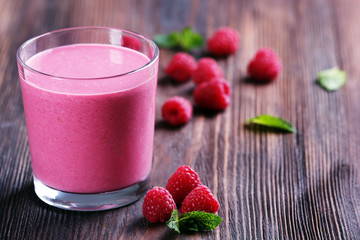 Glass of raspberry milk shake with berries on wooden background