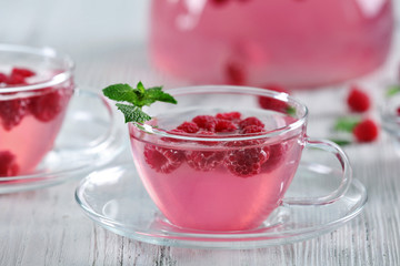 Cups and teapot of raspberry drink with berries on wooden table close up