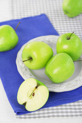 Green apples in plate on table with napkin, closeup