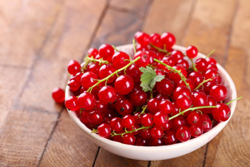 Fresh red currants in bowl on wooden table close up