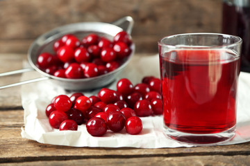 Glass with cherry juice on table, on wooden background