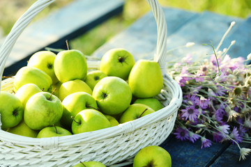 Green apples with bouquet of wildflowers on wooden table, closeup