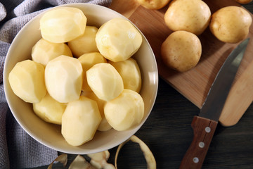Peeled new potatoes in bowl on wooden table with napkin, closeup