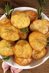 Delicious baked potato with rosemary in bowl on table close up