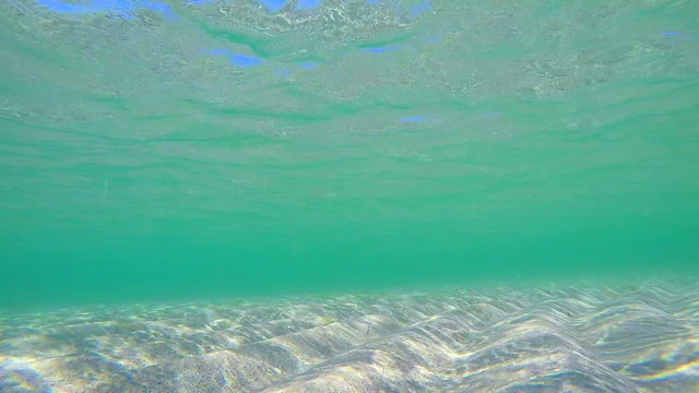 Shallow sand seabed with sunlight through turquoise water surface underwater
