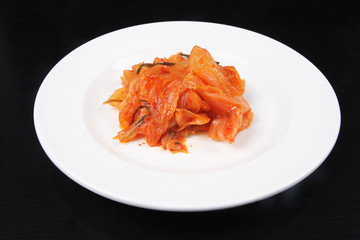 Kimchi on white plate against black background