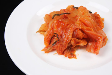 Kimchi on white plate against black background