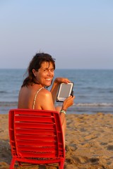 beautiful smiling woman reads the ebook on the beach