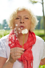 Seniorin pustet Pusteblume im Sommer