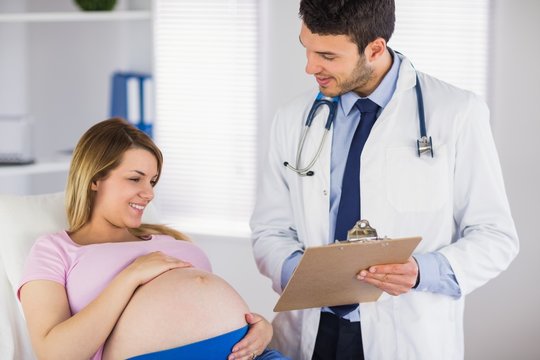 Smiling doctor giving advice to lying pregnant patient