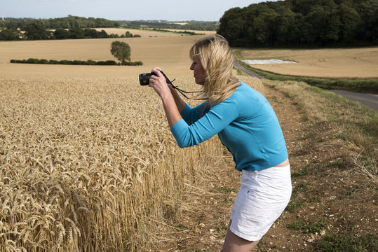 Woman using a digital camera to photograph a field of wheat