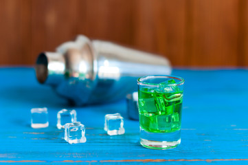 Close-up green alcohol cocktail with cubes of ice and shaker on