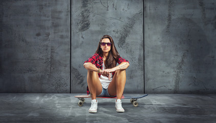 junge frau sitz auf skateboard vor leerer Wand