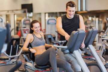 happy woman with trainer on exercise bike in gym