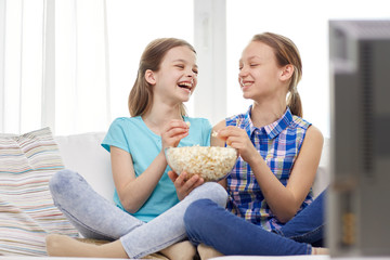 happy girls with popcorn watching tv at home