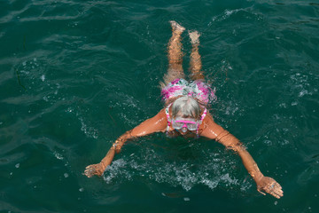 Aged woman is swimming with goggles in the sea.