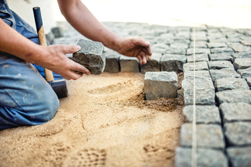 construction worker placing stone tiles in sand for pavement, terrace. Worker placing granite...