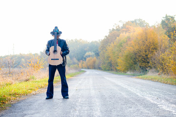 Man holding guitar with both hands on country road.