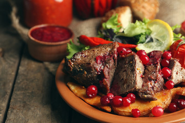 Tasty roasted meat with cranberry sauce, salad and roasted vegetables on plate, on wooden background