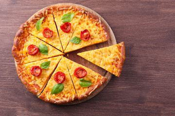 Slices of tasty cheese pizza with basil and cherry tomatoes on table close up